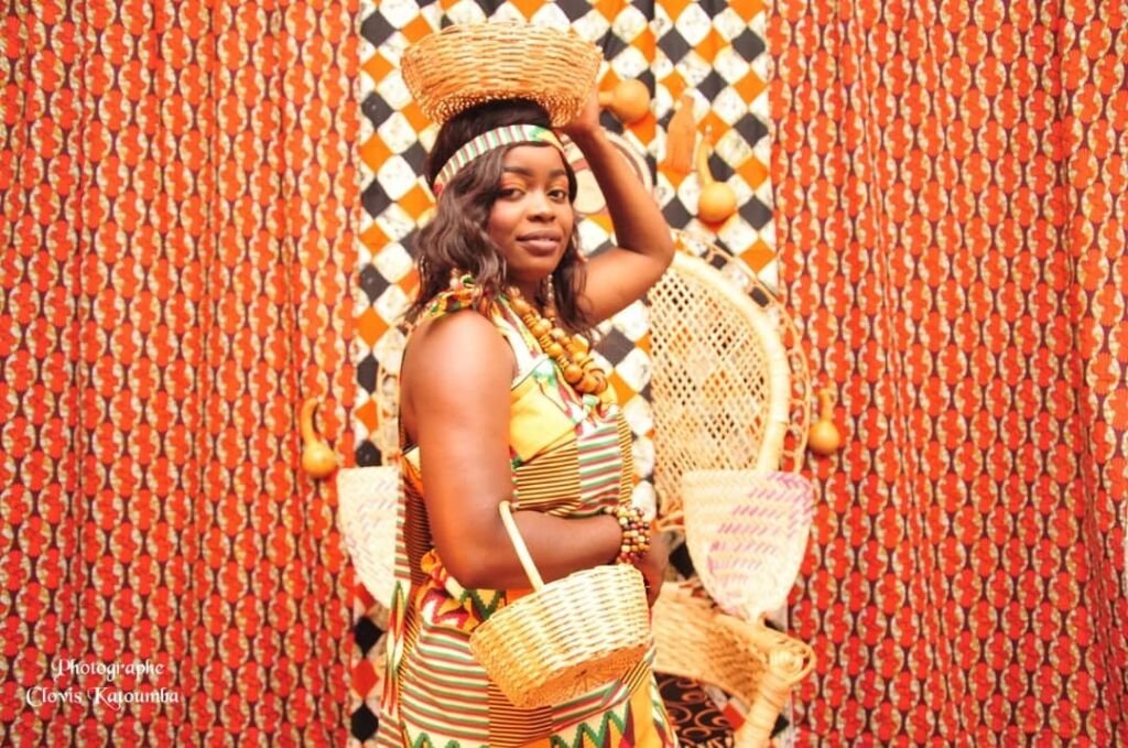 A woman in traditional African attire balances a basket on her head and carries another.