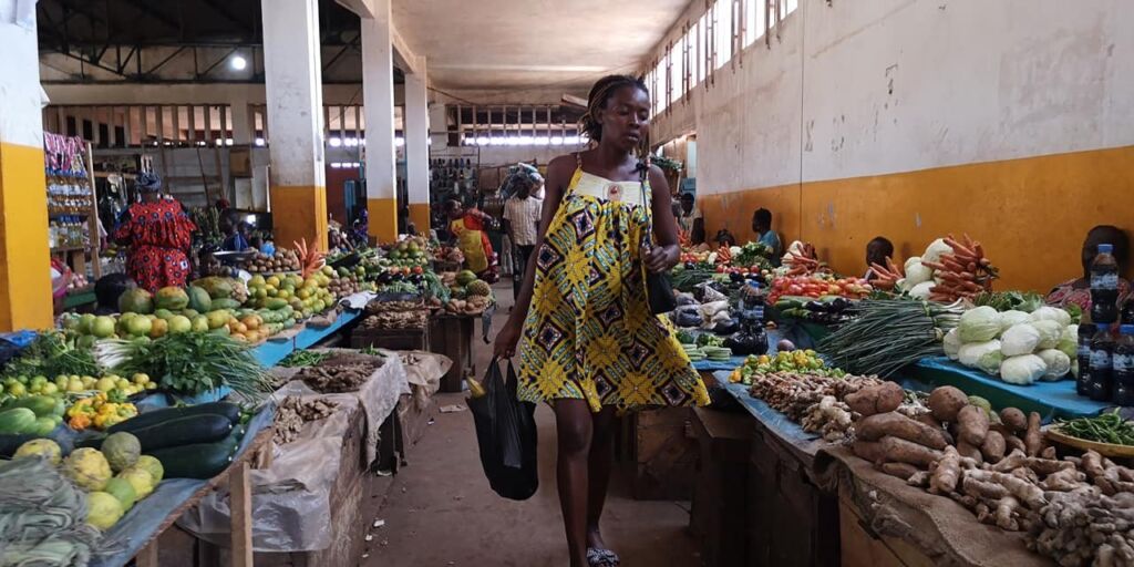 A woman walks through a vibrant African market filled with colorful produce.