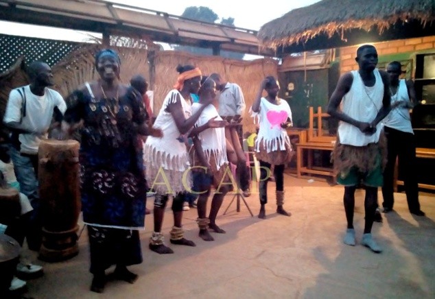 A group of people perform a traditional dance with drums outside a building.
