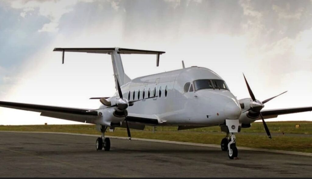 A white turboprop aircraft sits on a tarmac under a cloudy sky.