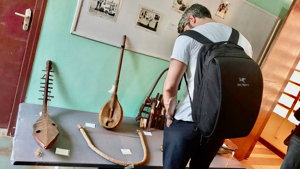 A person with a backpack is looking at an exhibit of old musical instruments on a table in a museum.