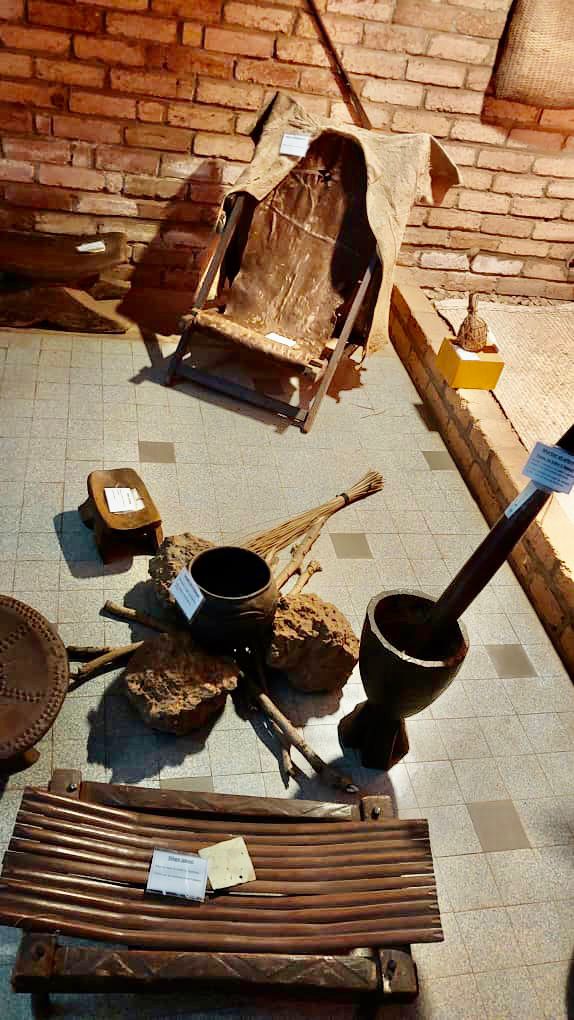 A high-angle shot of a museum display featuring traditional African tools, including a wooden chair, grinding pot, and an instrument with slats.